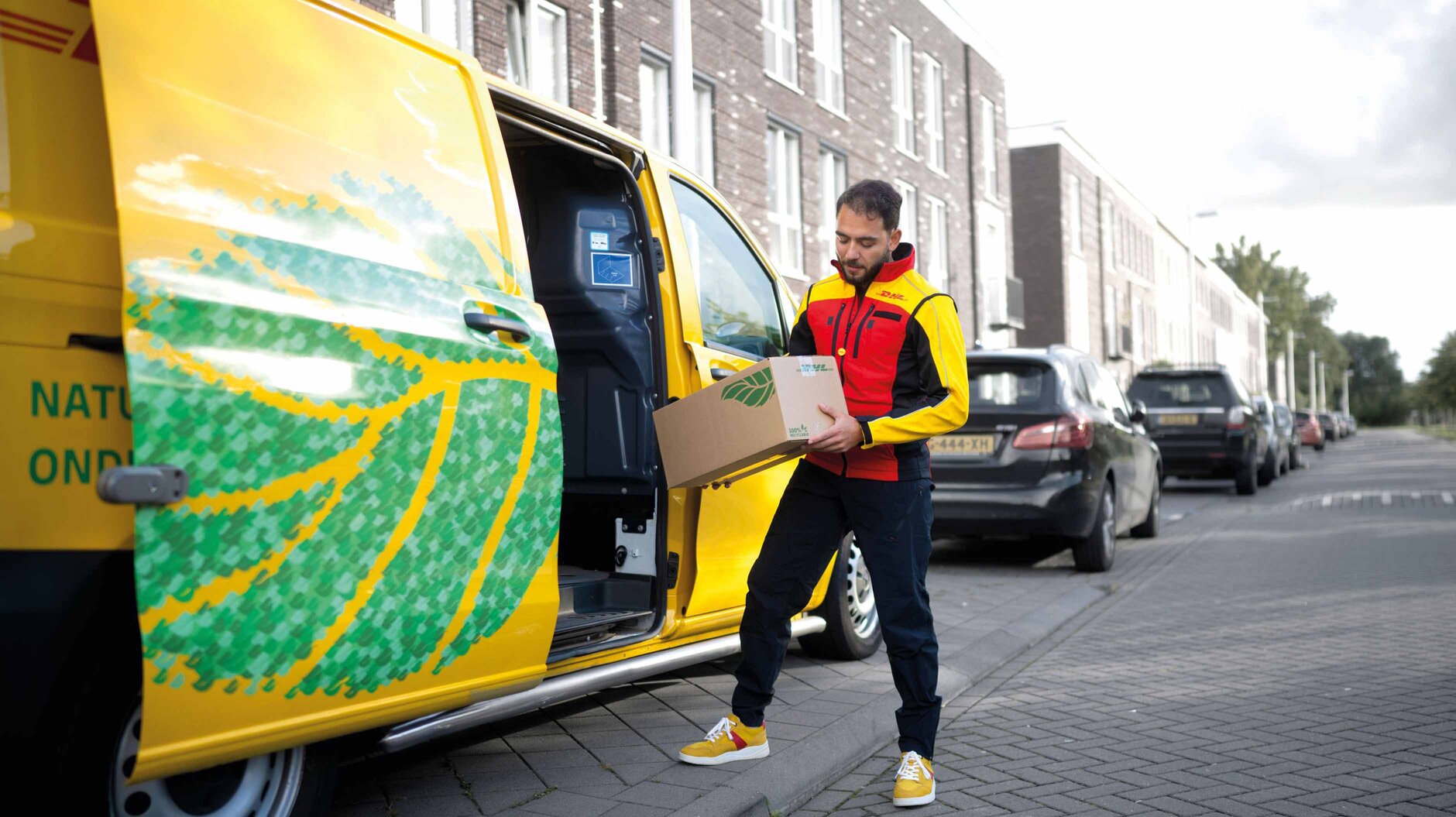 DHL-bezorger met pakket bij een elektrische bestelbus